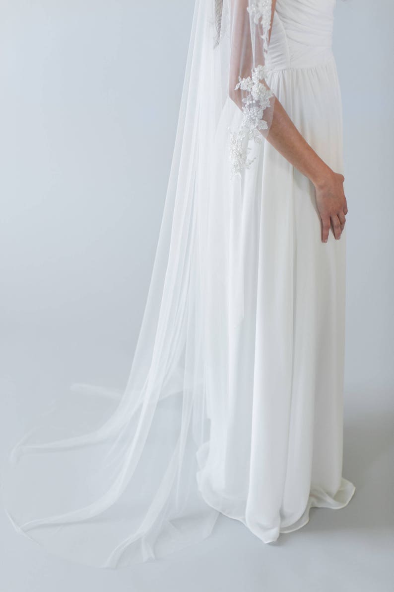 Puede incluir: Un velo de novia blanco con delicados detalles de encaje en los bordes. El velo est&aacute; hecho de una tela suave y transparente y tiene un dise&ntilde;o fluido y elegante.