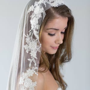 Puede incluir: Un velo de novia blanco con un delicado borde de encaje floral. El velo est&aacute; hecho de tul suave y presenta un delicado patr&oacute;n floral.