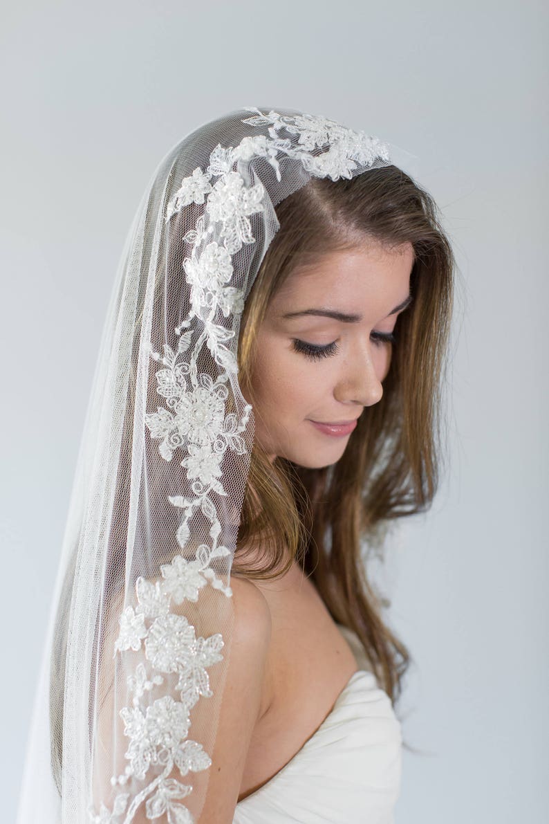 Puede incluir: Un velo de novia blanco con un delicado borde de encaje floral. El velo est&aacute; hecho de tul suave y presenta un delicado patr&oacute;n floral.