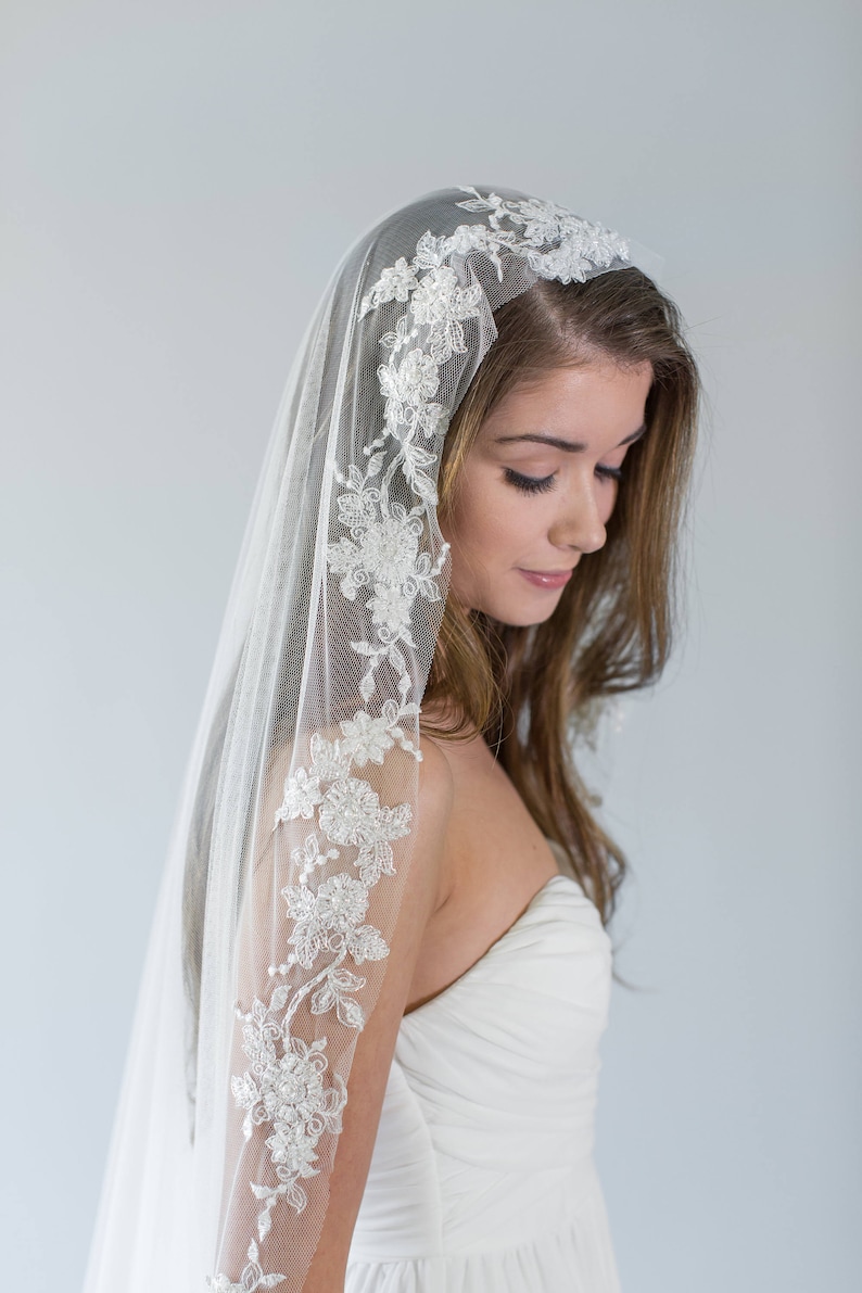 Puede incluir: Un velo de novia blanco con un delicado borde de encaje floral. El velo est&aacute; hecho de tul suave y tiene una sola capa.