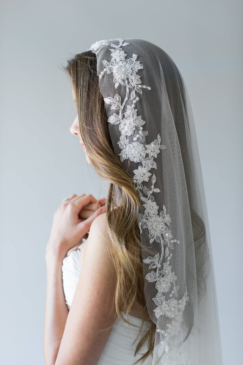 Puede incluir: Un velo de novia blanco con un delicado borde de encaje floral. El velo est&aacute; hecho de tul suave y es perfecto para un look de boda simple y elegante.