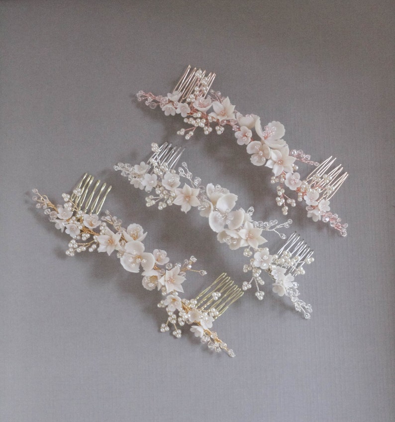 May include: Three hair combs with delicate floral designs. Each comb features a cluster of white and blush-colored flowers with pearl accents and crystal embellishments. The combs are arranged in a staggered pattern on a gray background.
