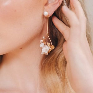 May include: Gold dangle earrings with a pearl at the top and a cluster of white flowers and leaves at the bottom.