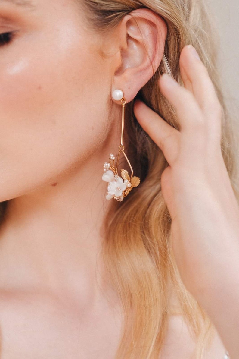 May include: Gold dangle earrings with a pearl at the top and a cluster of white flowers and leaves at the bottom.