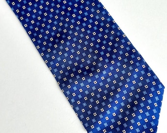May include: A blue tie with a repeating pattern of small white and blue squares. The tie is angled, showing its length and the detailed design. The background is a light, neutral color.
