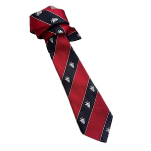 Może przedstawiać: Czerwono-czarny w paski krawat z powtarzającym się białym emblematem i rokiem 1863. Krawat jest zawiązany u góry i skierowany w dół, prezentując swój wzór. Krawat wykonany jest z gładkiego materiału, prawdopodobnie jedwabiu.