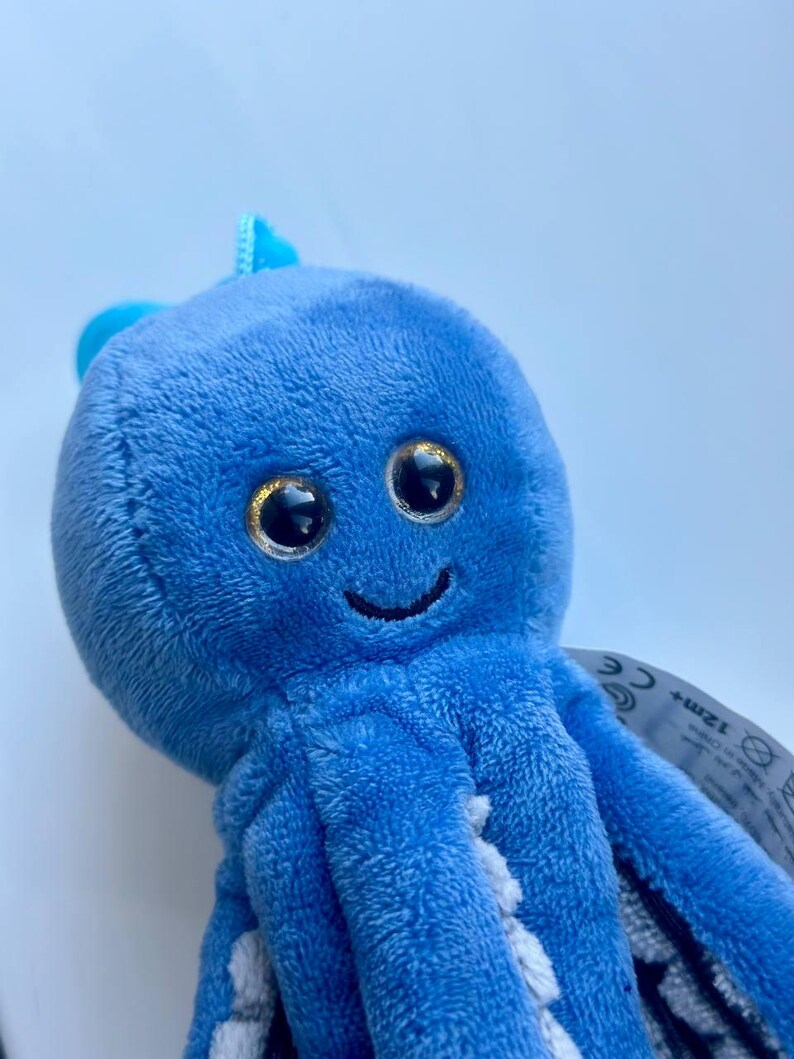 May include: A plush blue octopus toy with large, glittery eyes and a smiling mouth. The toy has eight tentacles and a small fin on top of its head. The toy is made of soft, fuzzy material.