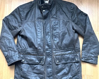 Puede incluir: Chaqueta de algodón encerado marrón oscuro con cuello alto y múltiples bolsillos. La chaqueta presenta una parte delantera abotonada, cintura con cordón y diseño de hombros acolchados. La chaqueta es de longitud media y tiene una estética robusta.