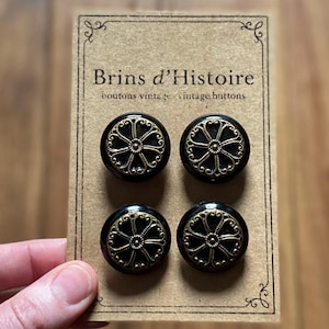 Peut inclure: Quatre boutons vintage noirs avec des motifs en filigrane dorés, présentés sur une carte marron. La carte porte l'inscription "Brins d'Histoire boutons vintage vintage buttons". Les boutons sont ronds et ont une finition brillante.