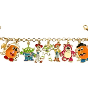 May include: Gold-toned charm bracelet featuring colorful enamel charms of characters from the animated film series. The charms include Mr. Potato Head, an alien, Jessie, Buzz Lightyear, Woody, Lotso, and another Mr. Potato Head.
