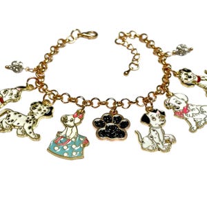 May include: Gold-coloured charm bracelet with Dalmatian dog charms and a black paw print charm. The charms are white with black spots and accents of red, pink, and blue. The bracelet has a lobster clasp closure.
