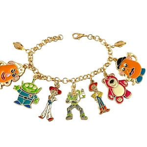 May include: A gold-colored charm bracelet featuring colorful enamel charms of characters from a popular animated movie. The charms include a green alien, a red bear, and a cowboy.