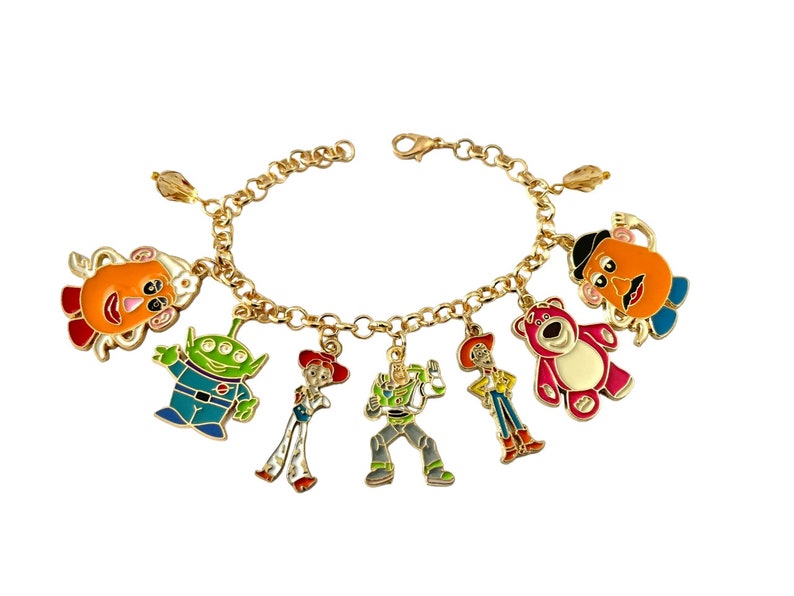 May include: A gold-colored charm bracelet featuring colorful enamel charms of characters from a popular animated movie. The charms include a green alien, a red bear, and a cowboy.