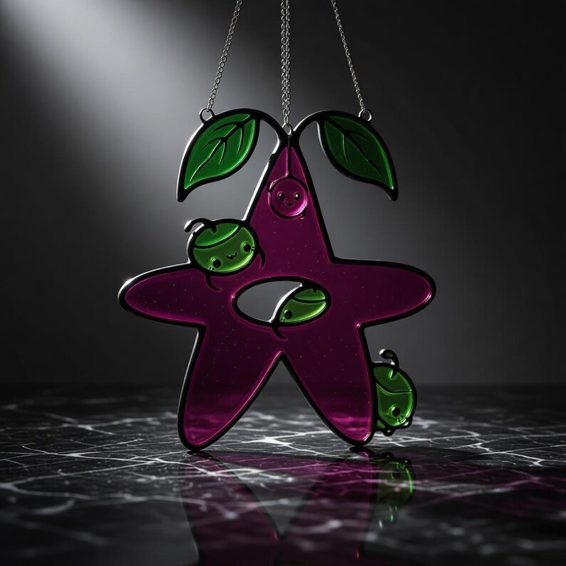 Op de afbeelding: Een magenta, stervormige glas-in-lood raamhanger met groene accenten. Het ontwerp toont groene bladeren en lachende kevers. De hanger hangt aan een zilveren ketting en is een speels decoratief element.