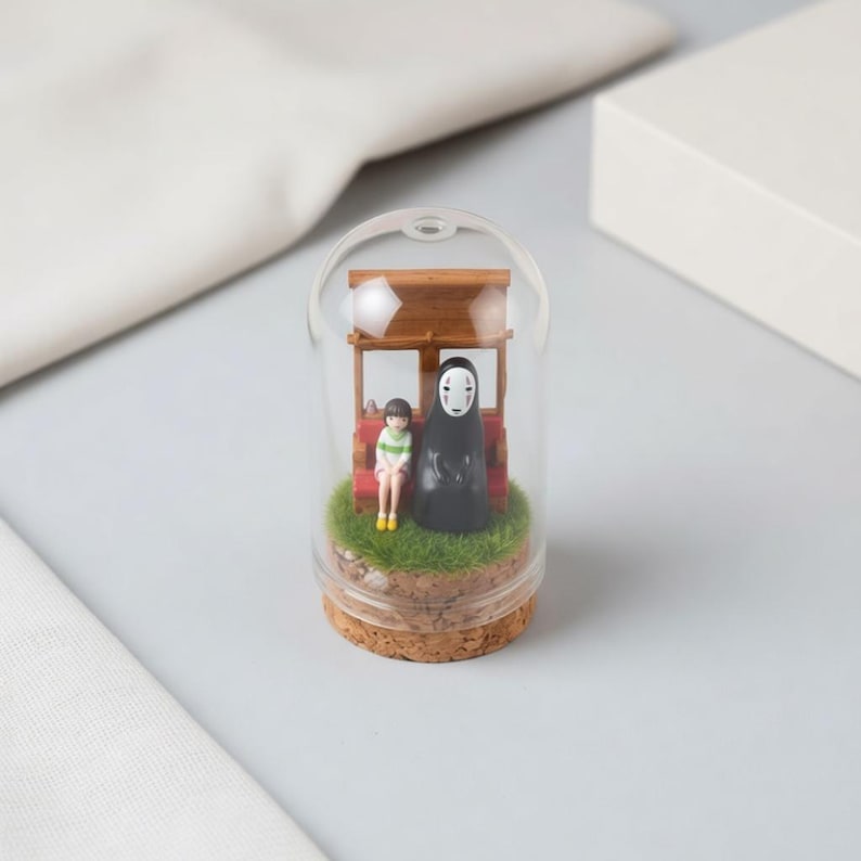 May include: A miniature diorama inside a clear glass dome. It features two figurines: a young girl and a tall, faceless figure, seated on a miniature wooden structure with a red bench. The base is a cork with artificial grass.