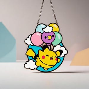 May include: A vibrant, cartoon-style hanging decoration. It depicts a yellow character with red cheeks, smiling, and floating with balloons. The balloons are pink, purple, yellow, and green, with white clouds. It is suspended by a chain.