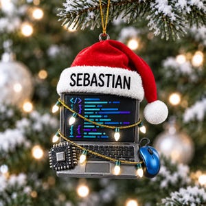 May include: A holiday ornament shaped like a laptop with a red Santa hat on top, featuring the name SEBASTIAN on the white brim. The screen displays blue code, and the laptop is wrapped in a string of small white lights with a blue computer mouse.