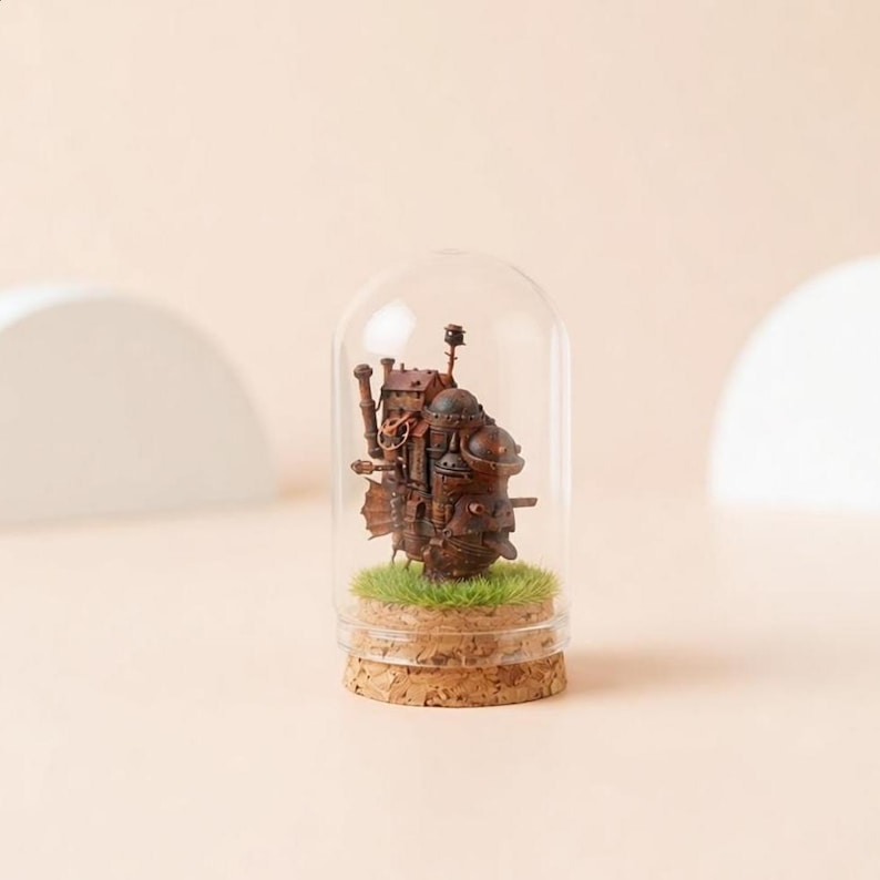 May include: A miniature brown steampunk-style castle sculpture inside a glass dome. The sculpture sits on a bed of green faux grass, with a cork base. The dome is clear, and the background is a soft beige.