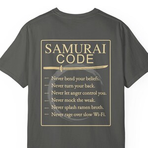 May include: Dark gray t-shirt featuring the text "SAMURAI CODE" in a rectangular frame, with a sword illustration. The text includes rules such as "Never bend your beliefs" and "Never rage over slow Wi-Fi."