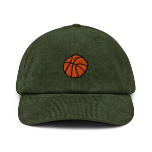 Könnte beinhalten: Eine grüne Cord-Baseballkappe mit einem aufgestickten orangefarbenen Basketball. Der Basketball hat schwarze Linien. Die Kappe hat einen gebogenen Schirm und eine runde Krone. Ein sportliches Accessoire.