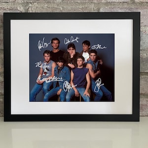 May include: Framed photograph featuring a group of young men in denim jackets and t-shirts, likely a cast photo. Each person's signature is visible on the image. The black frame is set against a brick wall.