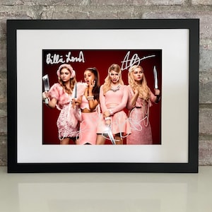 May include: Framed print featuring four women in pink outfits, each holding a knife. The background is red. The print has the text "Billie Lourd" and an autograph. The frame is black.