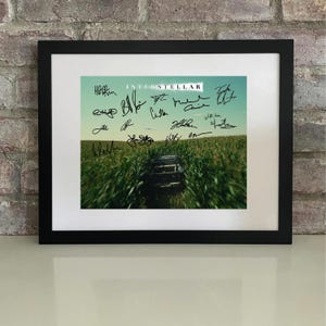 Puede incluir: Impresión enmarcada en negro con el título de la película "Interstellar" y firmas. La imagen muestra un campo de cultivos verdes que conduce a una estructura de madera bajo un cielo azul.