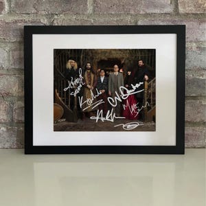 May include: Framed photograph featuring a group of people posing on a staircase. The photograph is in a black frame with a white mat. The image is signed in white ink.