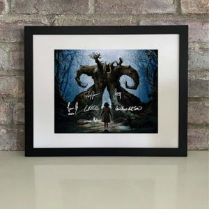 Puede incluir: Impresión artística enmarcada que representa una escena de fantasía con un niño frente a un gran árbol. La obra de arte está firmada. El marco es negro y la impresión tiene un borde blanco.