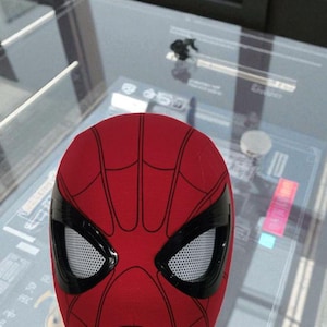 Puede incluir: Una m&aacute;scara roja de Spider-Man con telara&ntilde;as negras y marcos para los ojos. La m&aacute;scara es una toma de primer plano, mostrando el dise&ntilde;o ic&oacute;nico. Las lentes de los ojos son blancas con un patr&oacute;n de malla. Un art&iacute;culo tem&aacute;tico de superh&eacute;roes.