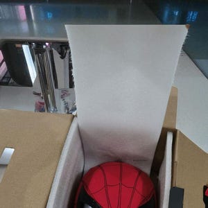 Puede incluir: Una m&aacute;scara roja de Spider-Man con detalles negros y ojos de malla blanca, empaquetada en una caja de cart&oacute;n con espuma protectora. La m&aacute;scara presenta un patr&oacute;n de telara&ntilde;a detallado.