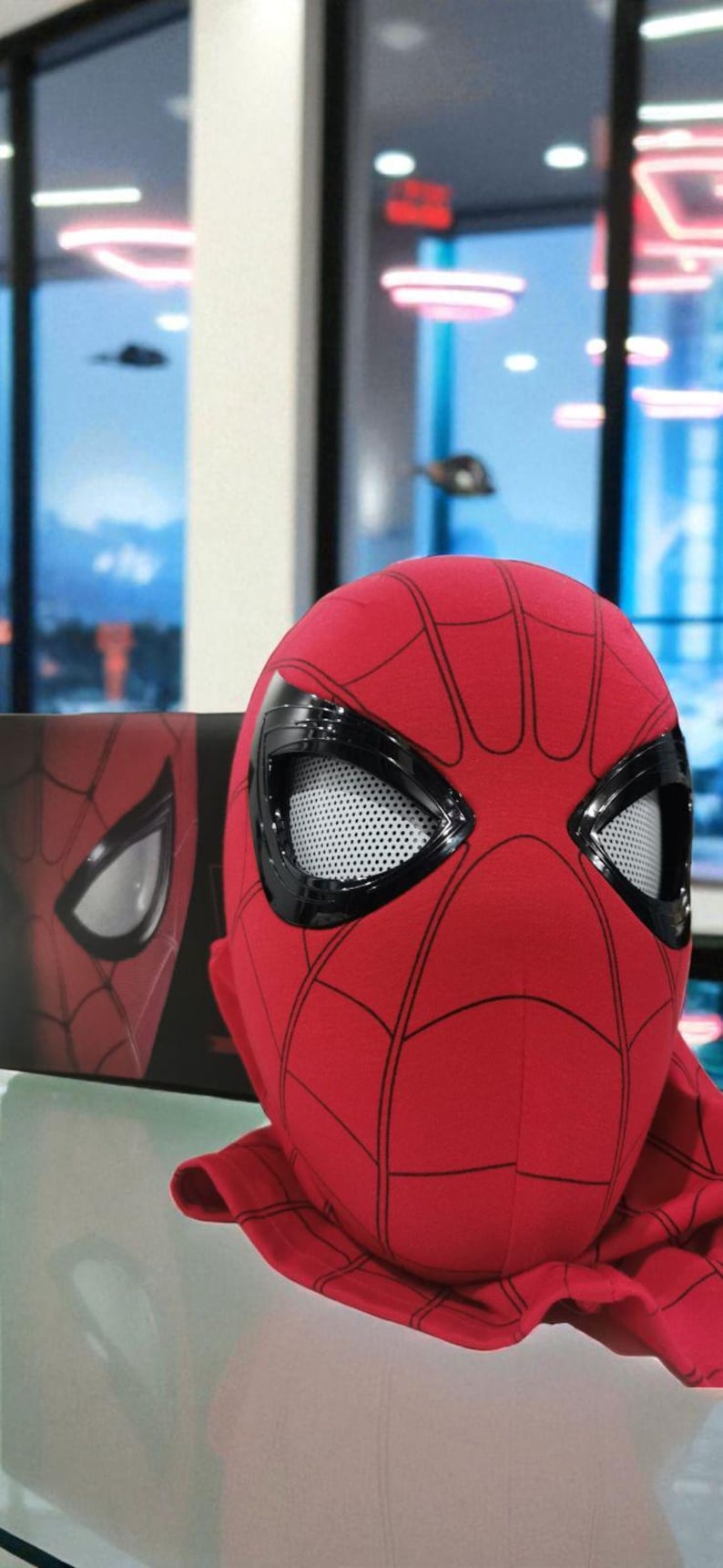 Puede incluir: Una m&aacute;scara roja de Spider-Man con telara&ntilde;as negras y marcos de ojos negros. Los ojos tienen un material de malla blanca. Una caja con una imagen similar est&aacute; a la izquierda. La m&aacute;scara es un disfraz de superh&eacute;roe.