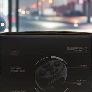 Puede incluir: Caja negra con el texto "HERO SERIES" y diagramas de un dispositivo con botones, etiquetados como "LEFT EYE", "RIGHT EYE", "SWITCH" y "CHARGING PORT". Tambi&eacute;n se muestra un cable de carga USB.