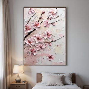 May include: A framed floral painting featuring textured, raised pink blossoms on dark branches against a light background. The artwork has a three-dimensional effect, with visible brushstrokes and a soft, pastel color palette. The painting is displayed in a bedroom setting.