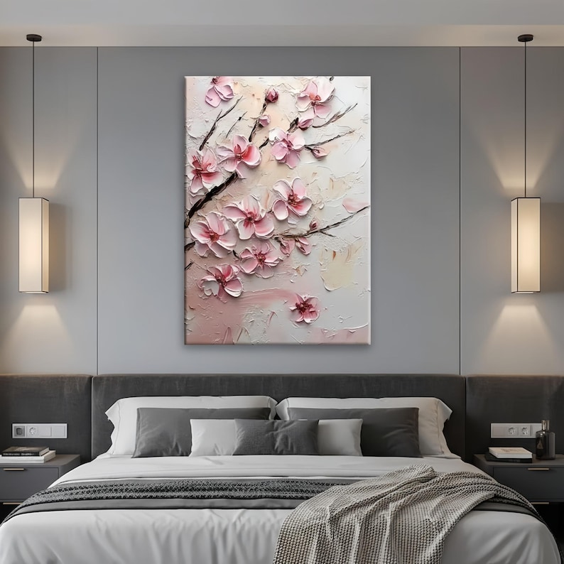May include: A textured canvas art piece featuring a close-up of pink cherry blossoms on dark branches. The flowers have a 3D effect, with a light pink and white background. The artwork is displayed above a bed.
