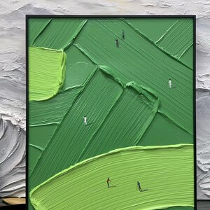 May include: Abstract oil painting of a golf course with a textured, green surface and a black frame. The artwork depicts golfers on the course, with varying shades of green and a white and grey background.