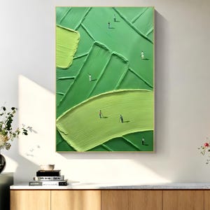 May include: Abstract green painting with textured brushstrokes and tiny figures. The artwork features varying shades of green, creating a sense of depth and movement. The painting is framed in a gold-colored frame and is displayed on a white wall.