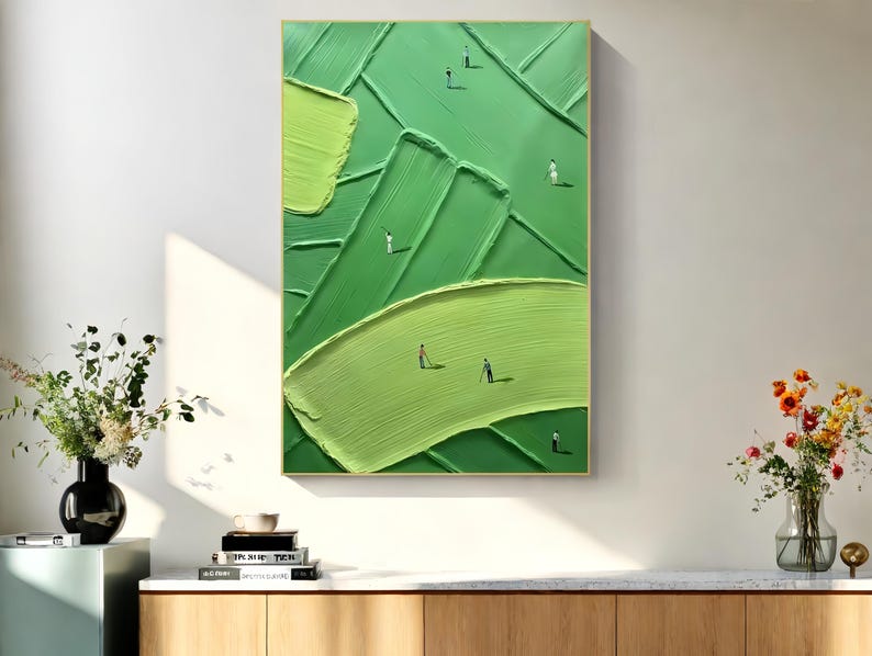 May include: Abstract green painting with textured brushstrokes and tiny figures. The artwork features varying shades of green, creating a sense of depth and movement. The painting is framed in a gold-colored frame and is displayed on a white wall.