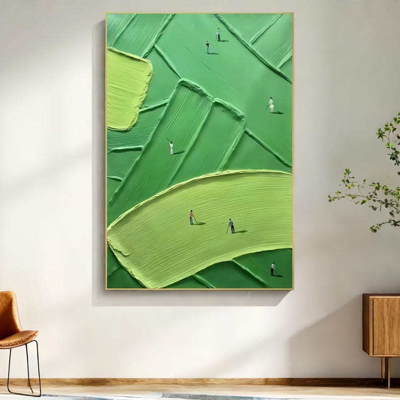 May include: Abstract painting of a golf course in shades of green, featuring textured brushstrokes and small golfer figures. The artwork is framed in a gold frame and hangs on a white wall.