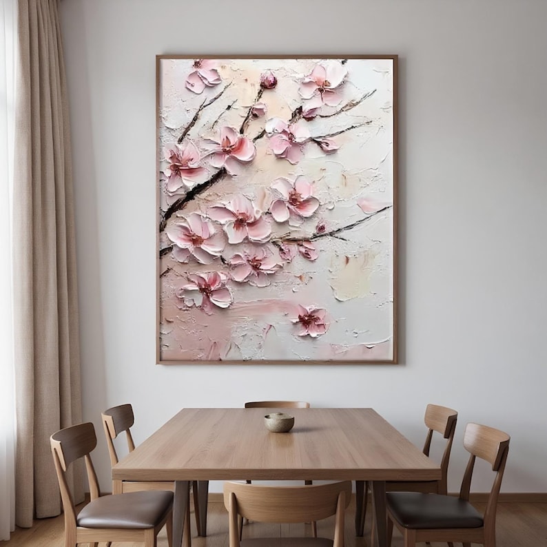 May include: A framed floral painting featuring textured, three-dimensional pink blossoms on dark branches. The artwork has a light pink and white background with visible brushstrokes. The painting is displayed above a wooden dining table.
