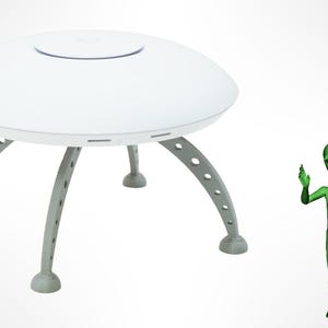 May include: A white, disc-shaped object with a raised circular center and four curved, grey legs featuring circular cutouts. Beside the disc stands a small, green, humanoid figure with a large head, almond-shaped eyes, and a slender body.