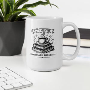 Pode incluir: Caneca de café de cerâmica branca com um gráfico a preto e branco. O gráfico apresenta uma chávena de café em cima de livros, com a palavra "COFFEE" por cima e "UNRESOLVED THOUGHTS" por baixo. A caneca está numa superfície branca.