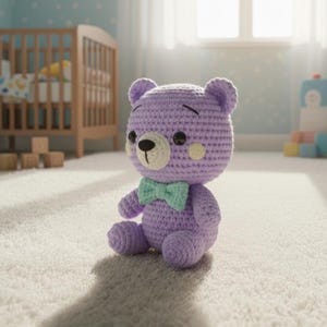 May include: A handmade, lavender crochet teddy bear with a mint green bow tie. The bear has black button eyes, a cream-colored snout, and small, round, peach-colored cheeks. It is sitting on a white carpet in a nursery setting.