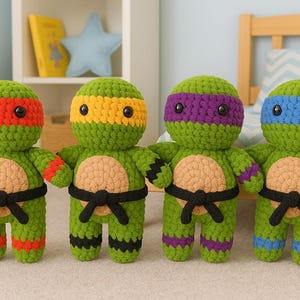 May include: Four handmade crochet dolls resembling Teenage Mutant Ninja Turtles. Each doll is green with a different coloured mask: red, yellow, purple, and blue. They have tan bellies, black belts, and matching coloured accents on their limbs.