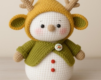 Puede incluir: Un muñeco de nieve de ganchillo hecho a mano que lleva una capucha de color amarillo mostaza con cuernos y una chaqueta verde. El muñeco de nieve tiene un cierre de botón, mejillas rosadas y dos botones rojos en la barriga. Decoración festiva.