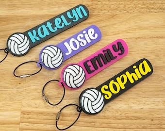 May include: Four personalized volleyball keychains in black, purple, pink, and yellow. Each keychain features a volleyball design and a name: Katelyn, Josie, Emily, and Sophia. The keychains have a black loop.