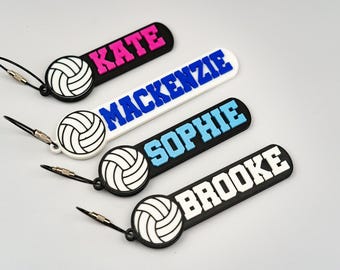 May include: Four personalized volleyball bag tags with names: Kate, Mackenzie, Sophie, and Brooke. Each tag has a volleyball graphic and a name in bold letters. The tags are black, white, and pink, with a silver loop.