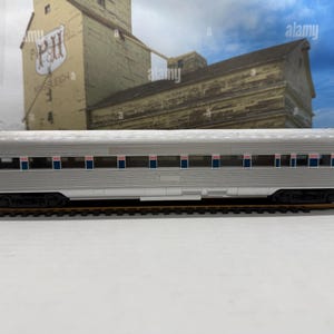 May include: A silver model passenger train coach car with a corrugated metal texture. The side features a horizontal blue and red stripe pattern, the number 7600 on the left, and the word Coach on the right. It sits on a brown model train track.