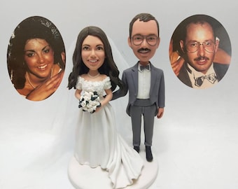 May include: A wedding cake topper featuring a bride and groom bobblehead, with two oval portraits on either side. The bride wears a white gown and veil, holding a bouquet. The groom is in a gray suit. The base is white with the date 1989.8.26.