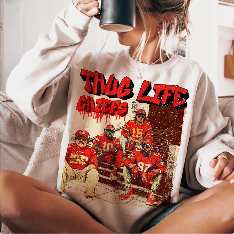 May include: White sweatshirt featuring a graphic of four football players in red uniforms, with the words "THUG LIFE CHIEFS" in red. The design has a vintage, distressed look.